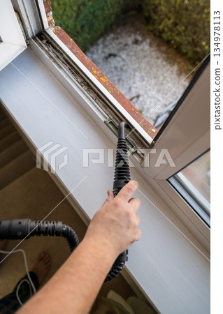 Cleaning the window. A man with steam device removes dirt from the plastic window frame. Cleaning the window. A man with steam device removes dirt from the plastic window frame. 134978113