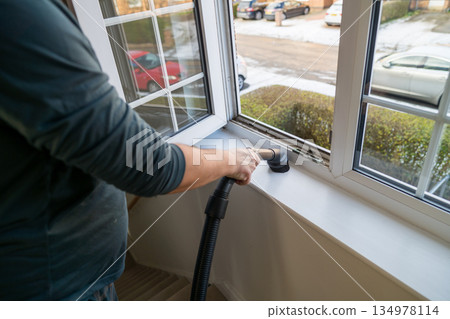 Spring home cleaning. Man vacuums plastic window frame. Spring home cleaning. Man vacuums plastic window frame. 134978114