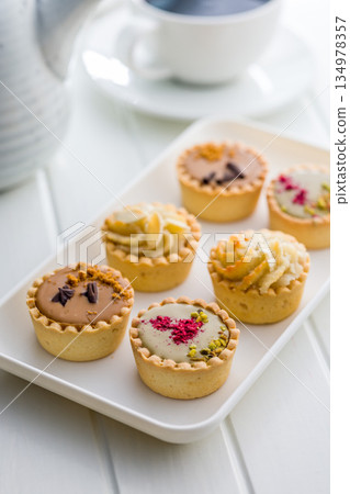 Sweet mini tartlets on plate on white table. Sweet mini tartlets on plate on white table. 134978357