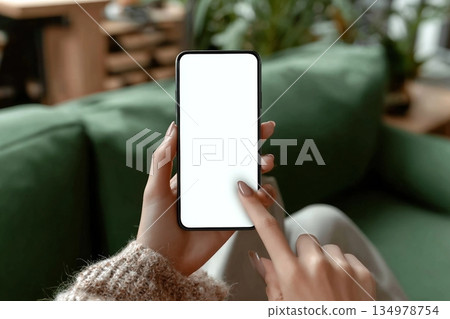 Close up of woman hand pointing on blank screen smartphone sitting on green sofa in cafe or lounge. Advertising Mockup, Social Media, Modern tech. 134978754