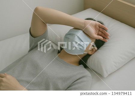 一張照片顯示，一名戴著口罩、身體不適的人躺在床上休息。 134979411