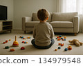 Back view of a child sitting in front of scattered toys 134979548