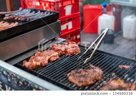 Close up view of grill at christmas market stall with sausages and meat cooking over hot coals, street food scene with smoke, heat and traditional winter festive atmosphere 134980336