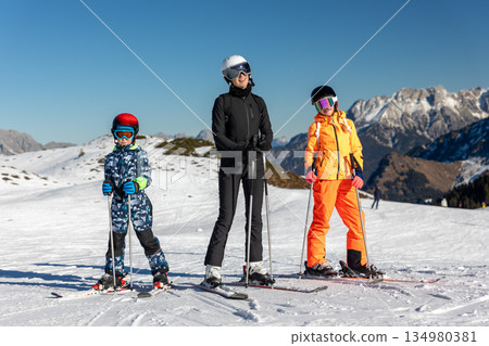 Family skiing together alpine slope children parent wearing helmets winter gear under clear blue sky. Snowy mountains, ski resort atmosphere, leisure, sport and joyful winter vacation lifestyle 134980381