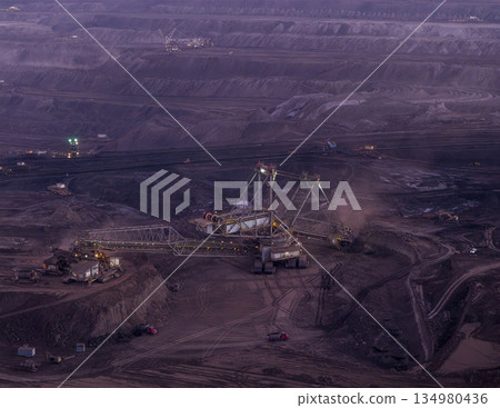 Panoramic view of an open pit coal mine with massive mining machines, layered terrain, and dramatic sky on the horizon. Powerful industrial landscape showing large scale extraction, energy production, 134980436
