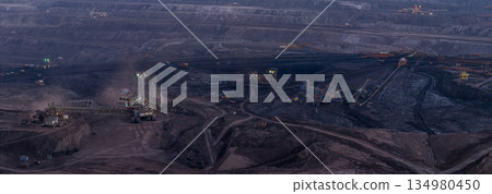 Ultra high resolution panoramic view of massive mining machines operating in an open pit coal mine, surrounded by dust and dramatic light. Powerful industrial scene showing large scale extraction, 134980450