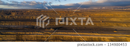 Ultra high resolution panoramic view of an open pit coal mine with massive mining machines, layered terrain, and dramatic sky on the horizon. Powerful industrial landscape showing large scale 134980453