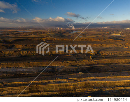 Ultra high resolution panoramic view of an open pit coal mine with massive mining machines, layered terrain, and dramatic sky on the horizon. Powerful industrial landscape showing large scale 134980454