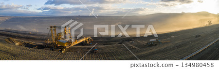 Ultra high resolution panoramic view of an open pit coal mine with massive mining machines, layered terrain, and dramatic sky on the horizon. Powerful industrial landscape showing large scale Ultra high resolution panoramic view of an open pit coal mine with massive mining machines, layered terrain, and dramatic sky on the horizon. Powerful industrial landscape showing large scale 134980458