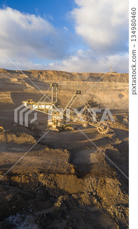 Panoramic view of an open pit coal mine with massive mining machines, layered terrain, and dramatic sky on the horizon. Powerful industrial landscape showing large scale extraction, energy production, Panoramic view of an open pit coal mine with massive mining machines, layered terrain, and dramatic sky on the horizon. Powerful industrial landscape showing large scale extraction, energy production, 134980460
