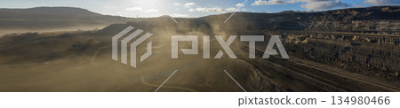 Ultra high resolution panoramic view of an open pit coal mine with massive mining machines, layered terrain, and dramatic sky on the horizon. Powerful industrial landscape showing large scale Ultra high resolution panoramic view of an open pit coal mine with massive mining machines, layered terrain, and dramatic sky on the horizon. Powerful industrial landscape showing large scale 134980466