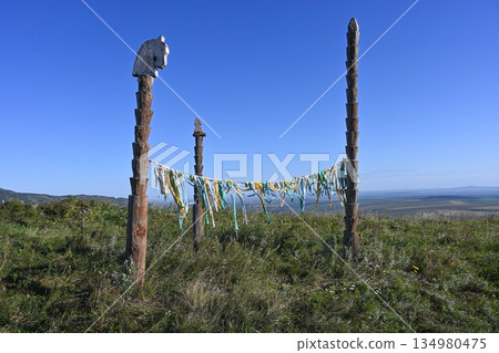 Ceremonial sacred ribbons are tied to wooden poles in the steppe against a blue sky background Ceremonial sacred ribbons are tied to wooden poles in the steppe against a blue sky background 134980475