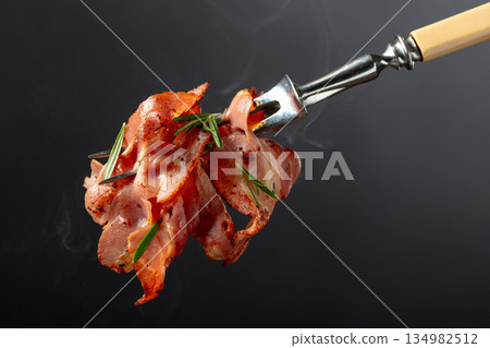 Hot fried bacon slices with rosemary on a fork. Hot fried bacon slices with rosemary on a fork. 134982512