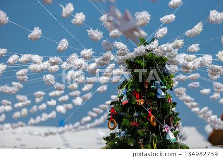 Colorful decorations adorn a Christmas tree with fluffy ornaments under a bright blue sky during the holiday season Colorful decorations adorn a Christmas tree with fluffy ornaments under a bright blue sky during the holiday season 134982739