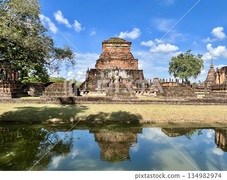 Wat Mahathat ruins and stone statues in Sukhothai Historical Park reflected in the water Wat Mahathat ruins and stone statues in Sukhothai Historical Park reflected in the water 134982974