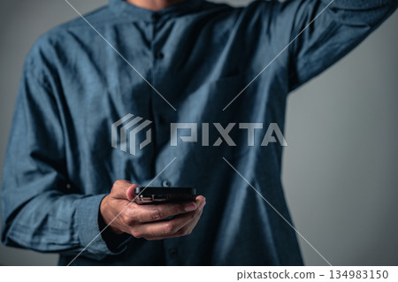 A man in a blue shirt holds a phone with one hand while using a gesture in a business pose, striking another pose for a studio portrait about technology and communication. A man in a blue shirt holds a phone with one hand while using a gesture in a business pose, striking another pose for a studio portrait about technology and communication. 134983150