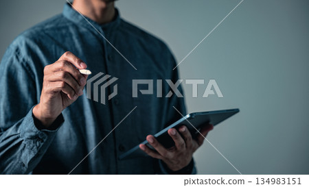 A man with pen in hand makes a sign gesture, a professional pose for business as he is posing with his tablet in a second thoughtful pose showing modern concepts. A man with pen in hand makes a sign gesture, a professional pose for business as he is posing with his tablet in a second thoughtful pose showing modern concepts. 134983151