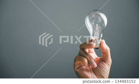 Hand holding a lightbulb against a gray background, symbolizing a new idea or solution. Hand holding a lightbulb against a gray background, symbolizing a new idea or solution. 134983152