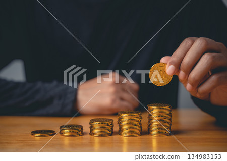 A closeup of a man hand pose and financial gesture, a clear sign of success while stacking gold coins as a good sign for investment, savings, and wealth management. A closeup of a man hand pose and financial gesture, a clear sign of success while stacking gold coins as a good sign for investment, savings, and wealth management. 134983153