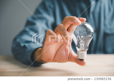 A closeup man hand pose and gesture holding a lightbulb is a creative sign of inspiration, a hopeful sign representing a brilliant new idea for business or technology. A closeup man hand pose and gesture holding a lightbulb is a creative sign of inspiration, a hopeful sign representing a brilliant new idea for business or technology. 134983156