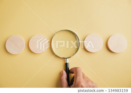 Closeup man hand pose shows a sign gesture for selection, holding a magnifying glass to find a candidate on a blank wooden sign representing human resource concepts. Closeup man hand pose shows a sign gesture for selection, holding a magnifying glass to find a candidate on a blank wooden sign representing human resource concepts. 134983159