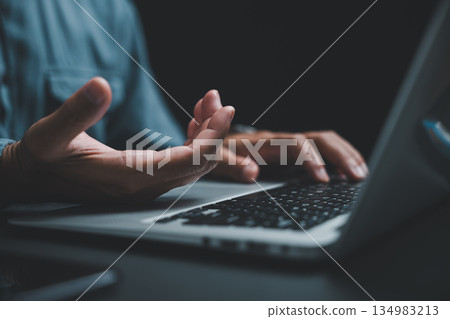 Close-up of hand gesturing over laptop keyboard, dark background. Close-up of hand gesturing over laptop keyboard, dark background. 134983213