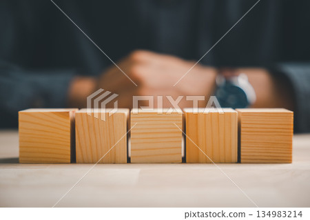 A closeup of a man hand posing a sign gesture behind blank wooden blocks, a conceptual five letter word sign for adding business text or creative icons on a wooden table. A closeup of a man hand posing a sign gesture behind blank wooden blocks, a conceptual five letter word sign for adding business text or creative icons on a wooden table. 134983214