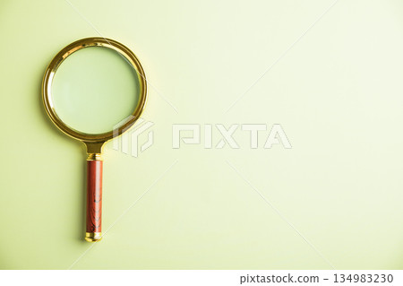 Golden magnifying glass with a wooden handle on a light green background. . Golden magnifying glass with a wooden handle on a light green background. . 134983230