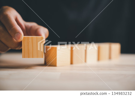 A conceptual sign of strategy, this closeup shows a man hand posing a gesture with a blank wooden block, a symbolic sign for building a new business foundation or plan. 134983232