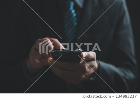 Close-up of hands holding a black smartphone with a blurred background of a person in a suit. 134983237