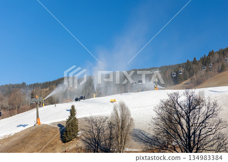 Austrian Alps ski resort shows strong contrast between white piste and snowless grass slope under blue sky. Climate warming, snow scarcity, chairlift infrastructure highlight winter tourism crisis Austrian Alps ski resort shows strong contrast between white piste and snowless grass slope under blue sky. Climate warming, snow scarcity, chairlift infrastructure highlight winter tourism crisis 134983384