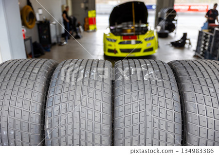 Racing tires aligned motorsport garage race car mechanics blurred background showing preparation performance focus. Professional pitlane environment emphasizes grip technology endurance competition 134983386
