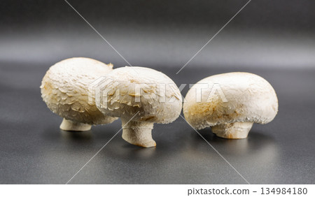 Three fresh white champignon mushrooms on gray surface closeup. 134984180