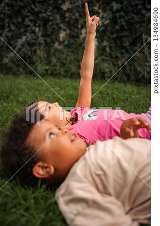 Children lying on grass pointing at sky exploring 134984690