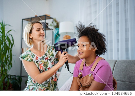Mother styling daughter's curly hair with a hairdryer at home Mother styling daughter's curly hair with a hairdryer at home 134984696