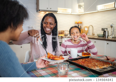 Mother serving pizza to daughters at family dinner 134984841