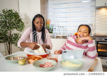 Mother and daughter baking homemade pizza in kitchen 134984853