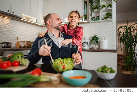 Father and daughter laughing while preparing healthy salad in kitchen Father and daughter laughing while preparing healthy salad in kitchen 134985093