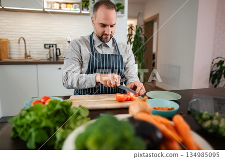 Man slicing fresh tomatoes preparing healthy meal in modern kitchen Man slicing fresh tomatoes preparing healthy meal in modern kitchen 134985095
