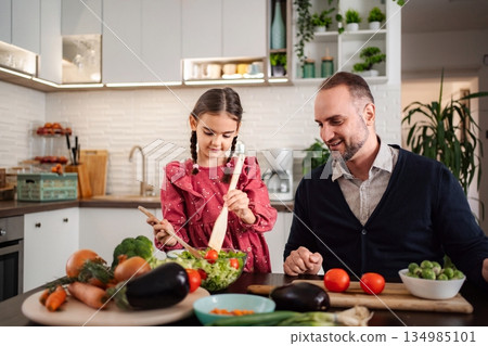 Father daughter cooking healthy vegetable salad in modern kitchen 134985101