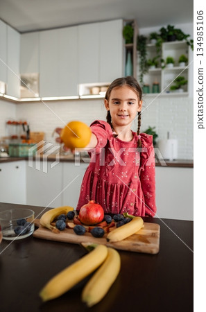 Girl holding lemon offering healthy snack in kitchen Girl holding lemon offering healthy snack in kitchen 134985106