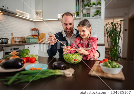Father and daughter preparing healthy fresh salad together in kitchen 134985107