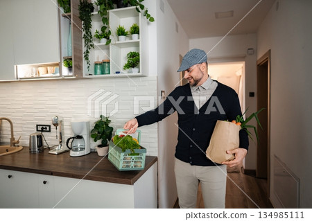 Delivery man unpacking fresh organic groceries in modern kitchen Delivery man unpacking fresh organic groceries in modern kitchen 134985111