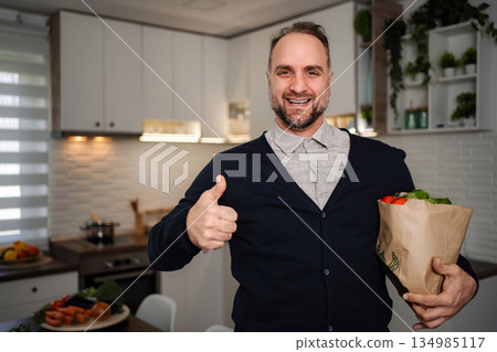 Happy man holding groceries bag in modern kitchen 134985117