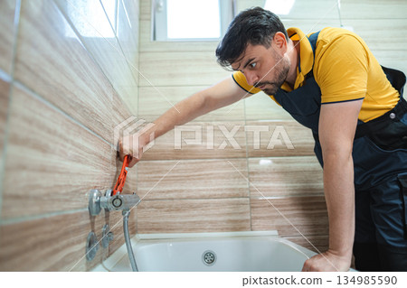 Plumber tightening faucet in bathroom using pipe wrench 134985590