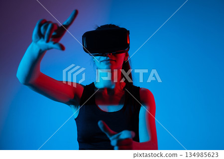 Young woman in VR headset using raised finger gesture for virtual interface interaction 134985623