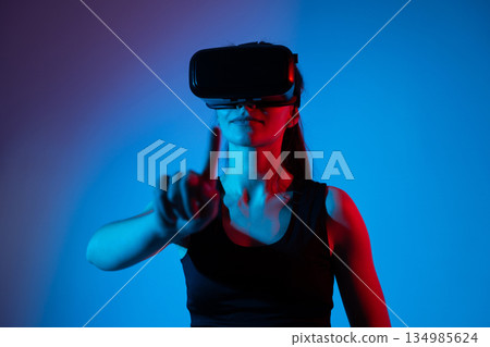 Woman wearing VR headset in red and blue neon lighting, immersive virtual reality experience concept Woman wearing VR headset in red and blue neon lighting, immersive virtual reality experience concept 134985624