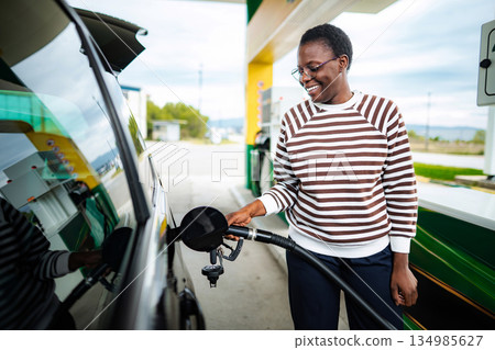 Young adult woman refueling her car at a gas station 134985627