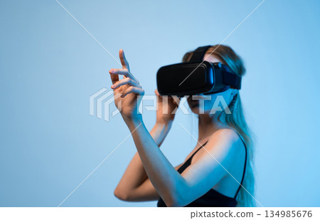 Young woman wearing VR headset and gesturing in virtual environment, immersive technology and digital future concept Young woman wearing VR headset and gesturing in virtual environment, immersive technology and digital future concept 134985676