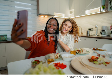 Diverse women taking selfie together in modern kitchen 134985680